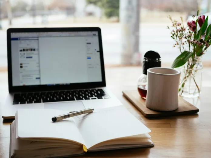 MacBook Pro with an open word processor, next to an open journal and a mug of coffee